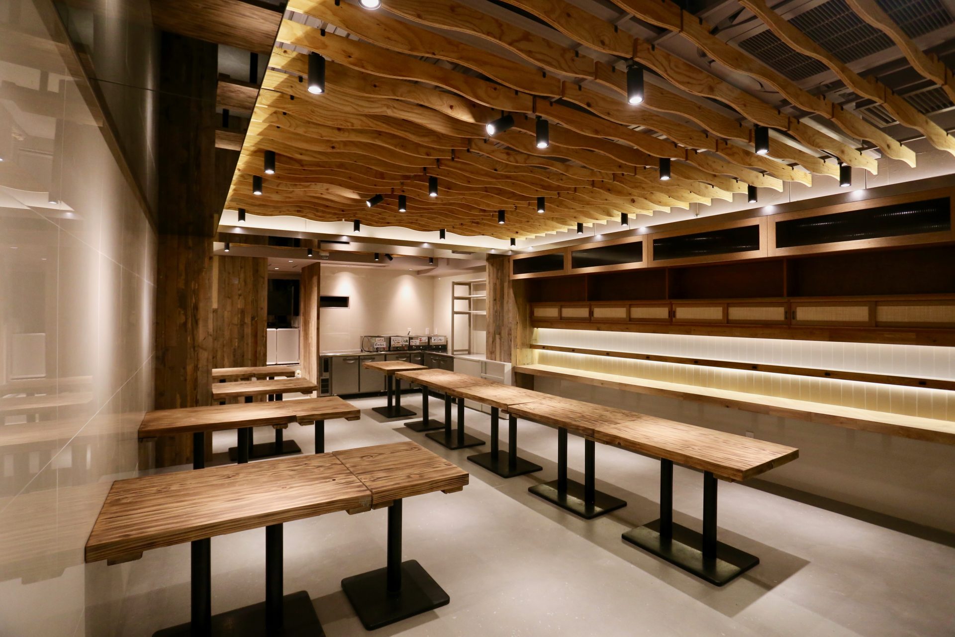 波形の木製天井と木のテーブル、間接照明を組み合わせたもうやんカレー大忍具店の内装